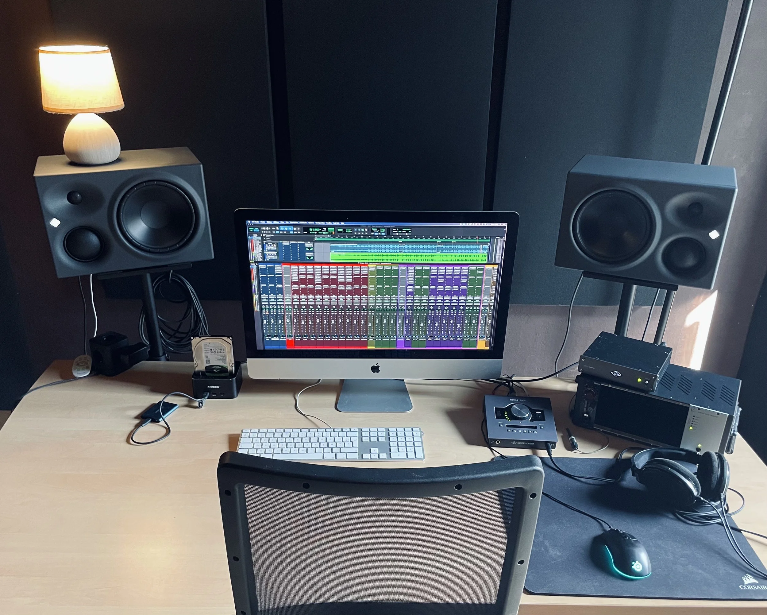 Studio d'enregistrement avec ordinateur affichant un logiciel de production audio, deux haut-parleurs, casque, contrôleurs, et autres équipements audio.